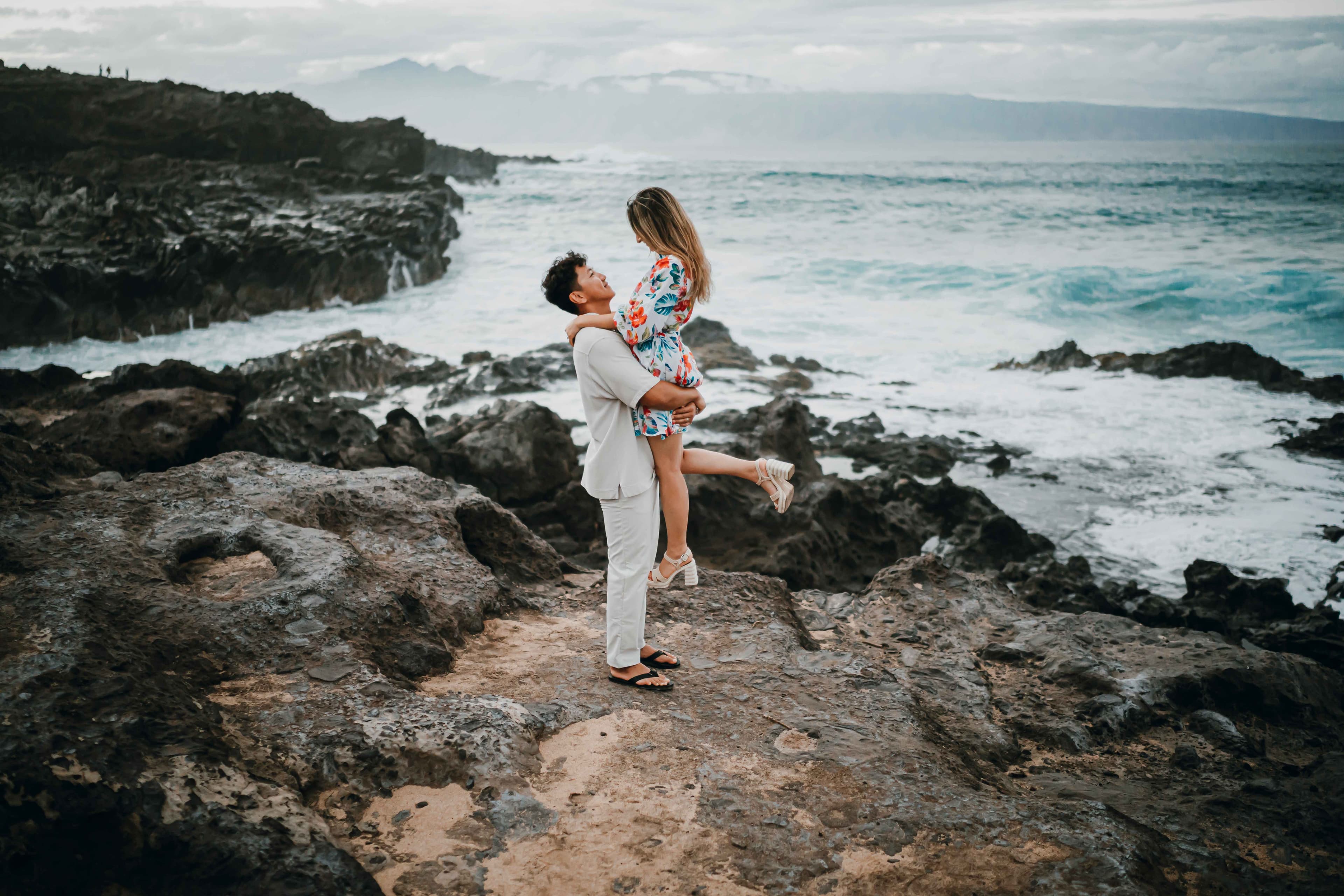 Playful couple on rocky coastline with crashing waves