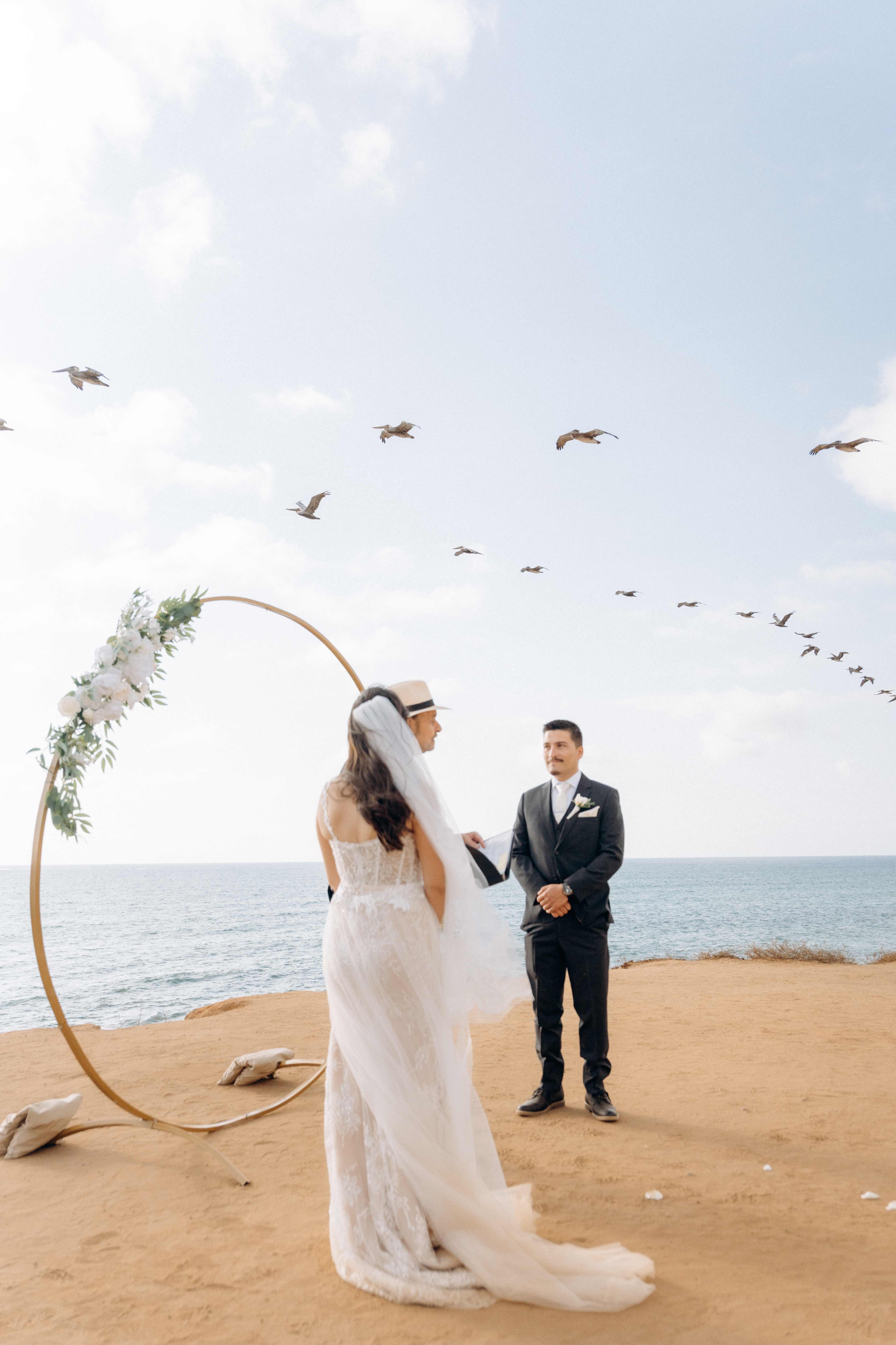 Beach ceremony with circular arch and birds flying over the ocean