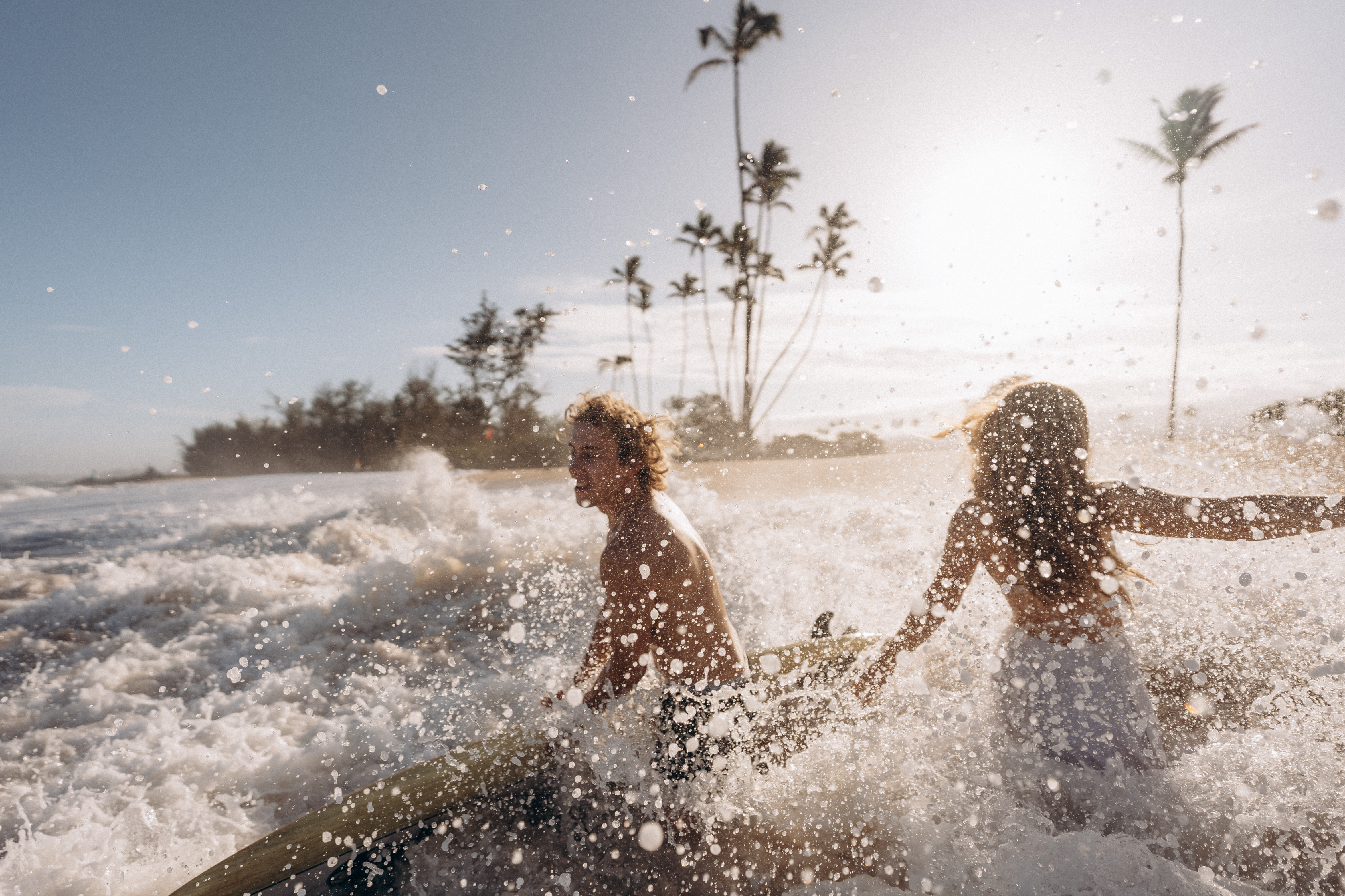 Couple splashing in ocean waves with palm trees at sunset